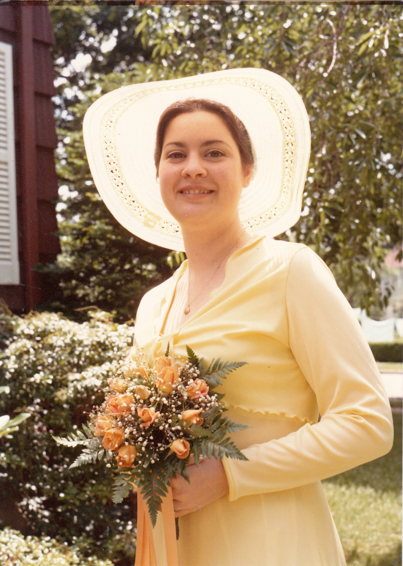 A young woman in a yellow dress and wide-brimmed hat, holding a bouquet